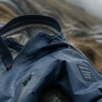 Veste gore tex femme sur pierre mouillée, capuche ouverte, reste au sec